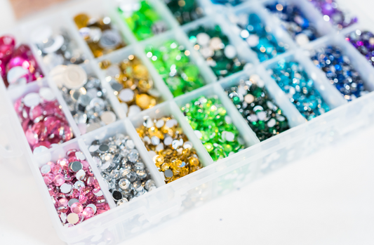 Various colored rhinestones in separate compartments, inside a clear box.