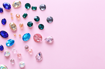 Many different colored rhinestones, scattered across a light pink surface.	