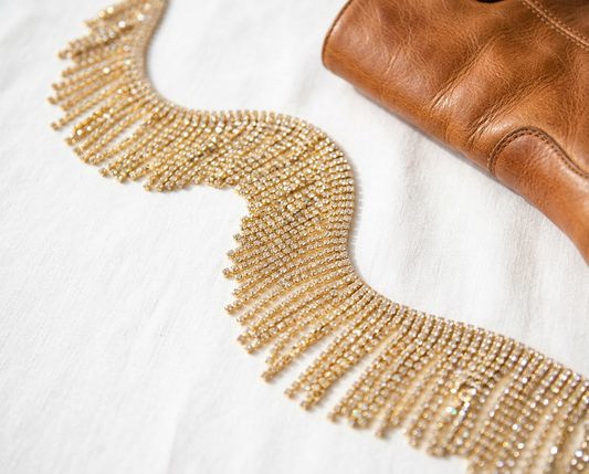 Gold rhinestone fringe trim displayed beside a brown leather accessory.