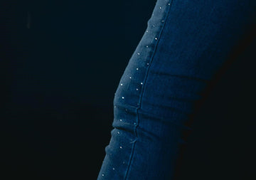 Close-up of dark jeans featuring scattered rhinestone accents against a dark background.