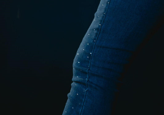 Close-up of dark jeans featuring scattered rhinestone accents against a dark background.