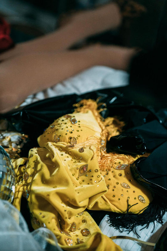 Close-up of yellow embellished fabric with rhinestones, gem accents, and decorative fringe details among black accessories.