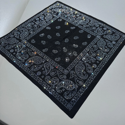 A black bandana laid flat, featuring an intricate paisley pattern entirely detailed with shimmering silver rhinestones.