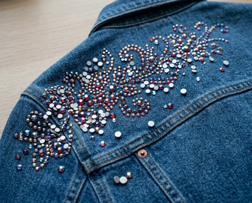 Multicolor rhinestones arranged in an ornate design on a blue denim jacket.