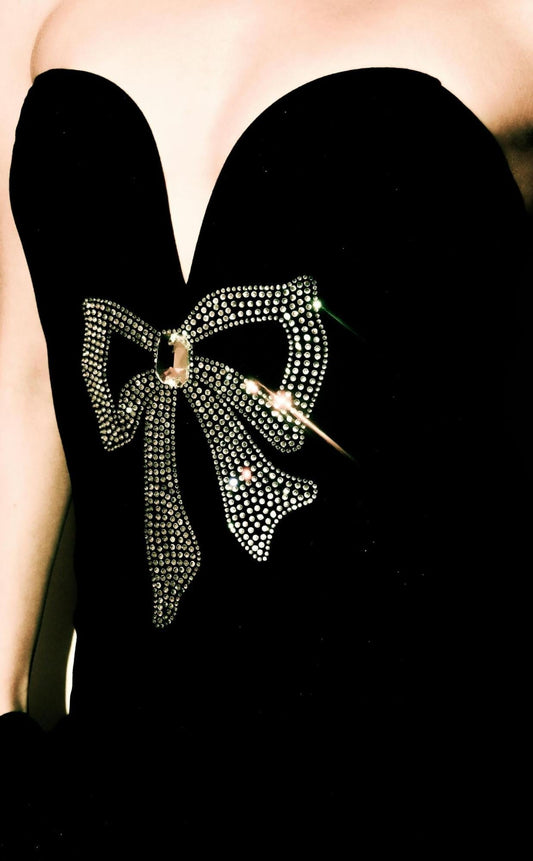 A close-up of a black strapless dress featuring a sparkling bow design made of small rhinestones and a large central gem.