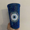 A travel cup covered in dark blue rhinestones, with an eye created from rhinestones on the front.